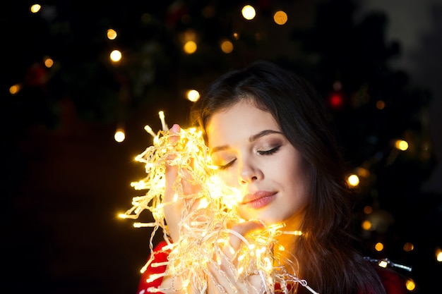 Beautiful young woman smiling and talking garlands of lights at home