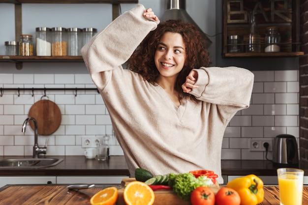 beautiful young woman smiling while cooking salad with fresh vegetables in kitchen interior at home