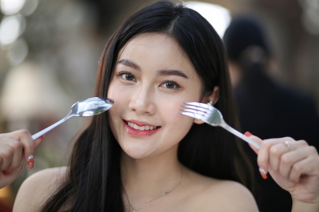 Beautiful young woman smiling while holding a spoon and a fork