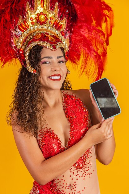 Beautiful young woman in special carnival feather costume holding a smartphone with blank screen with space for text. Virtual carnival, promotion and advertisements. Vertical