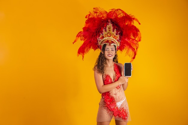 Bella giovane donna in costume speciale di piume di carnevale che tiene in mano uno smartphone con schermo vuoto con spazio per il testo. carnevale virtuale, promozione e pubblicità