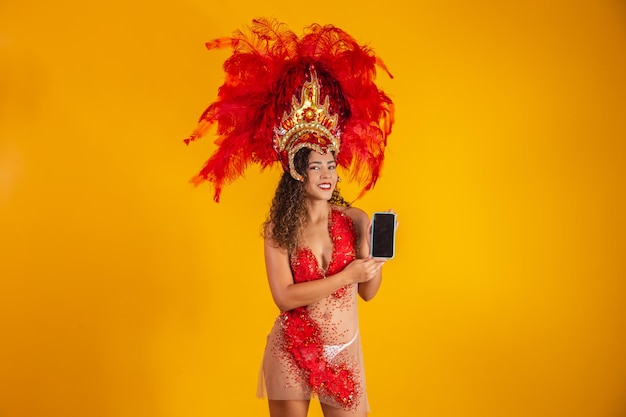 Beautiful young woman in special carnival feather costume holding a smartphone with blank screen with space for text. Virtual carnival, promotion and advertisements