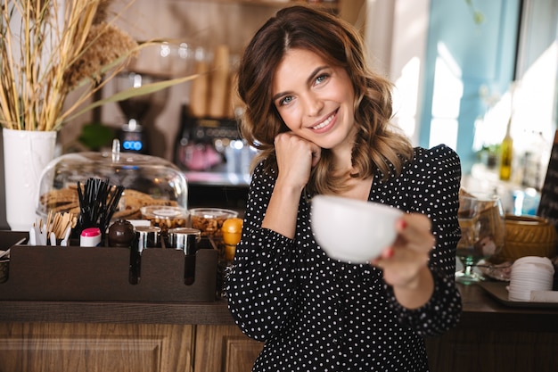 カップを持って、屋内のカフェで時間を過ごす美しい若い女性