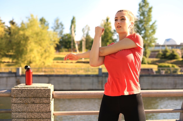 Foto bella giovane donna in abbigliamento sportivo che allunga le braccia e sembra concentrata mentre si trova sul ponte.