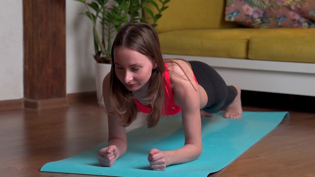 Beautiful young woman in sportswear doing plank exercises on a yoga mat in the evening at home.