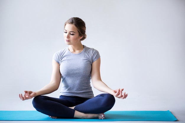 Beautiful young woman in sportswear practicing yoga while sitting in lotus position on gray background Yoga fitness and training
