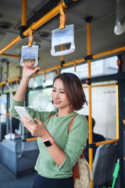 市バスに立って携帯電話を見ている美しい若い女性。