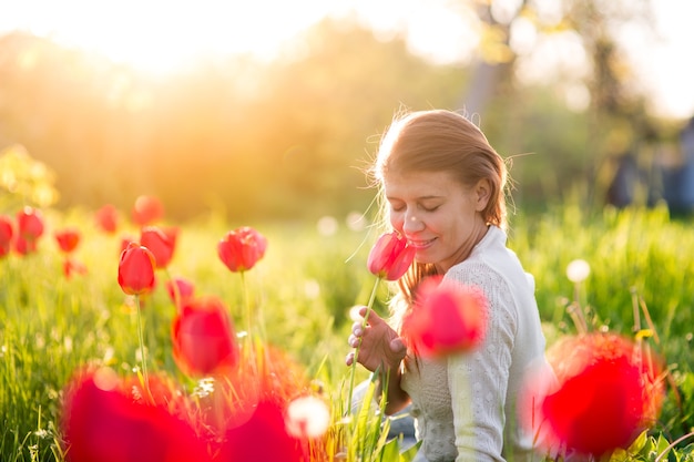 Bella giovane donna in piedi su una radura di erba verde con tulipani in fiore al tramonto