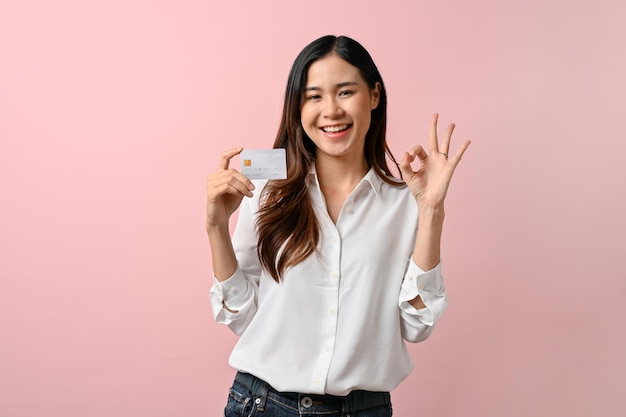 A beautiful young woman standing isolated over pink background holding credit card