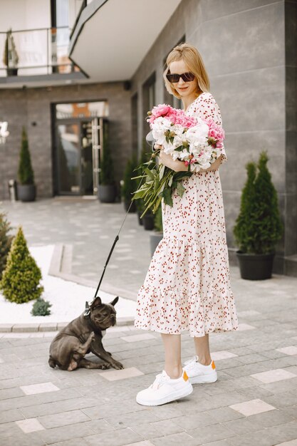 A beautiful young woman standing near cafe outdoors and holding bouquet of flowers. Woman wearing glasses and dress
