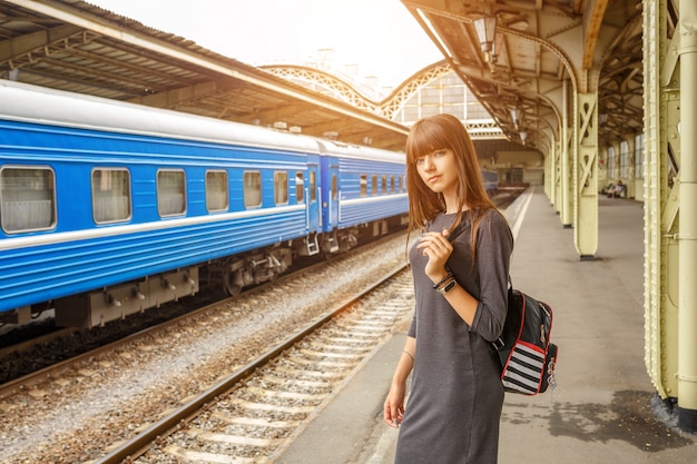 鉄道駅のプラットホームの上に立っている美しい若い女性。