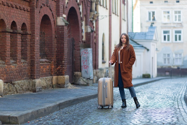 Beautiful young woman standing with a suitcase on the street of an unfamiliar city