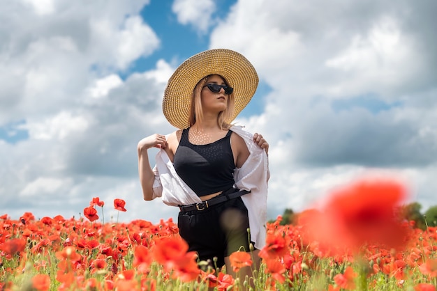 夏のポピー畑で麦わら帽子をかぶった美しい若い女性。美しさの自然