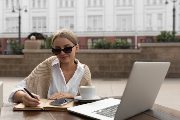 Beautiful young woman in a street cafe makes notes in a notebook