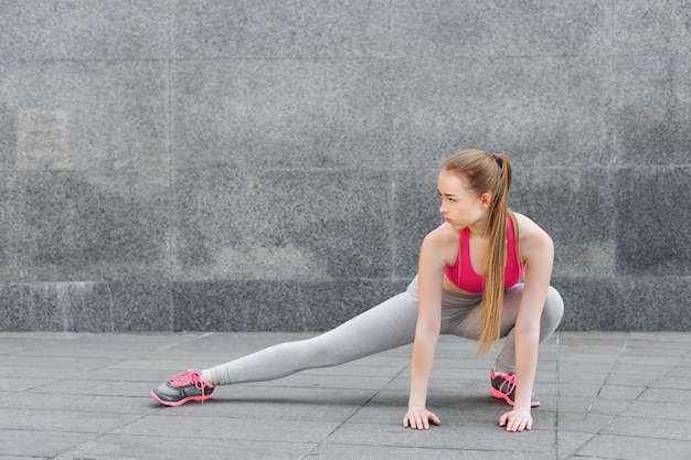 Beautiful young woman stretching against grey wall, preparing for training, copy space. Freedom spirit concept