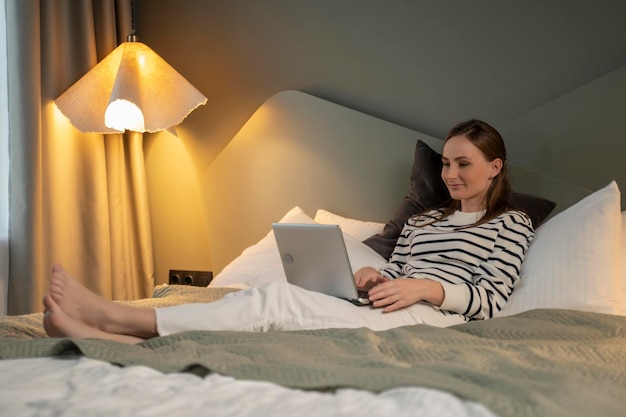 Beautiful young woman in a striped sweatshirt with a laptop is surfing the internet reading news on