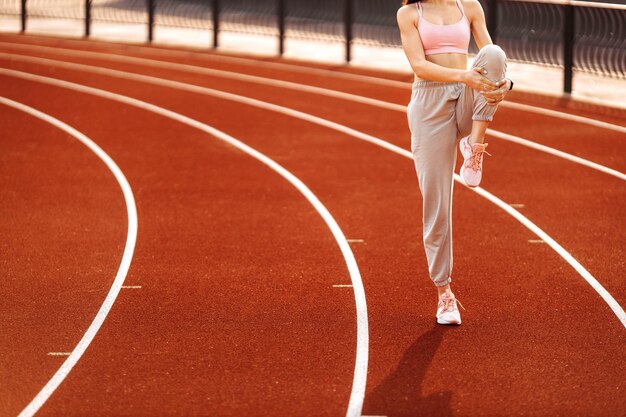 Beautiful young woman in stylish sportswear stretching out after workout at the stadium