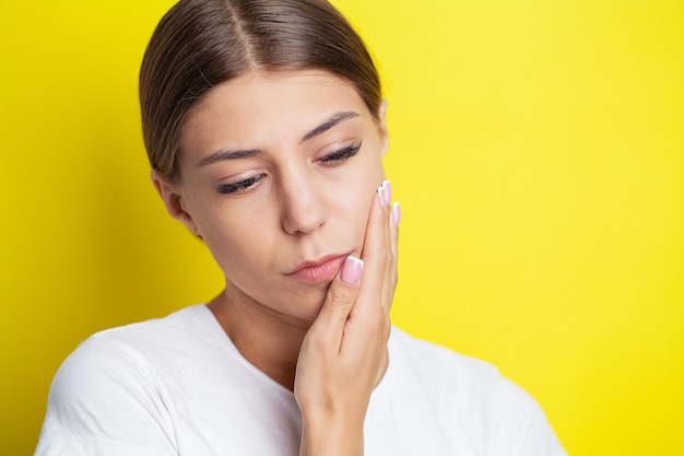 Beautiful young woman suffering from terrible severe toothache, touching cheek with hand