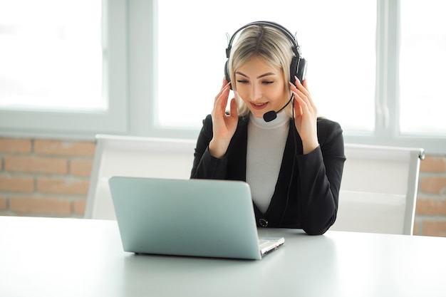 beautiful young woman in a suit in the office at the table with a laptop in headphones