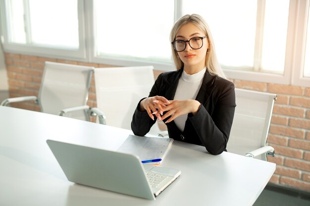 Foto bella giovane donna in un vestito in ufficio al tavolo con un computer portatile