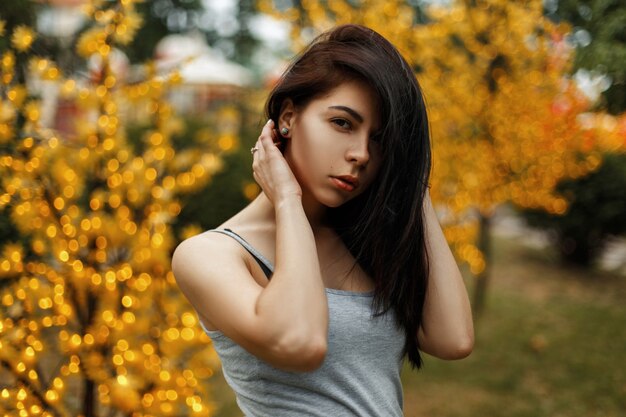 Beautiful young woman in summer clothes near a tree with lights in an amusement park