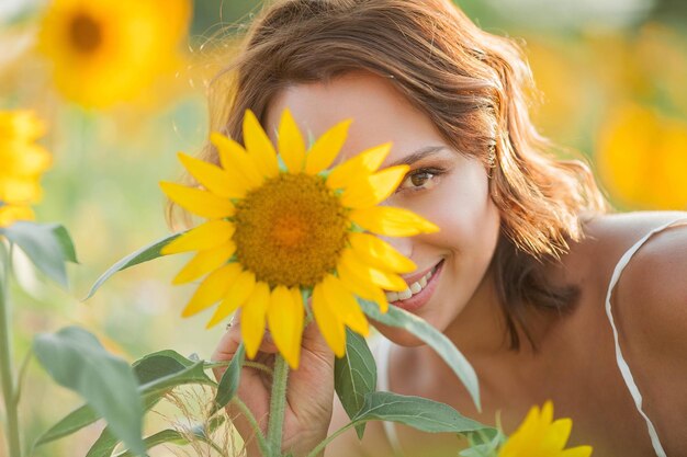 ひまわり畑の美しい若い女性。太陽の下で若い女性の肖像画。夏。