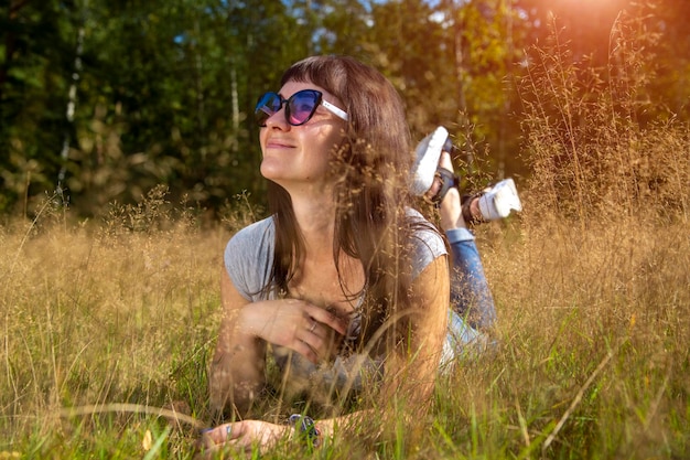 선글라스를 쓴 아름다운 젊은 여성은 따뜻한 햇살 아래 풀밭에서 태양을 즐긴다