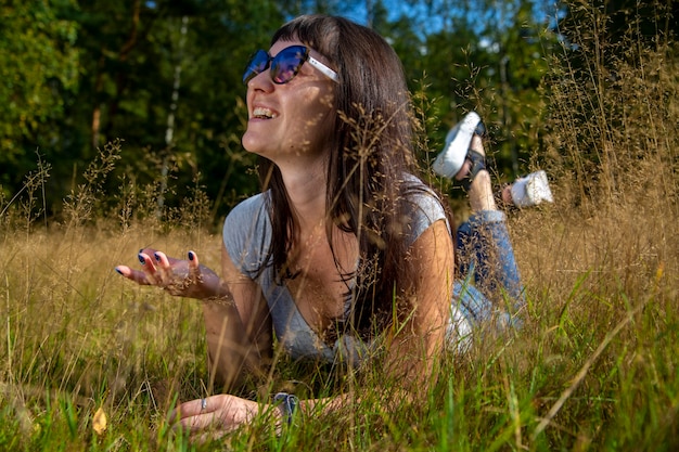 선글라스를 쓴 아름다운 젊은 여성은 풀밭에서 태양을 즐긴다