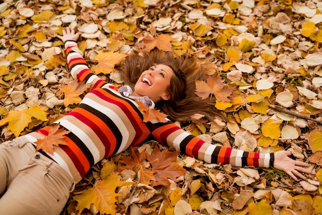 Beautiful young woman in sunny forest in autumn colors. She is lying on the fall meadow and enjoying.