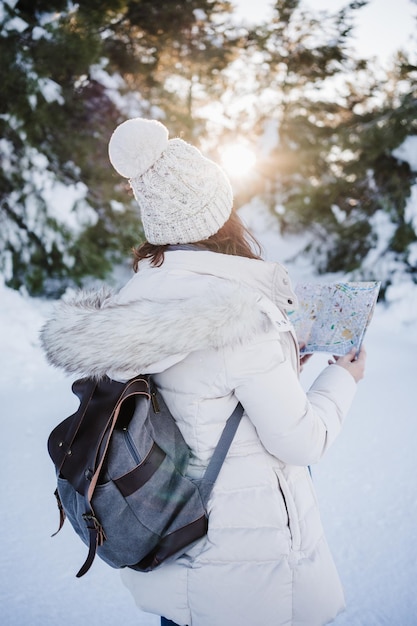 Beautiful young woman at sunset in snowy mountain reading a map travel nature and technology