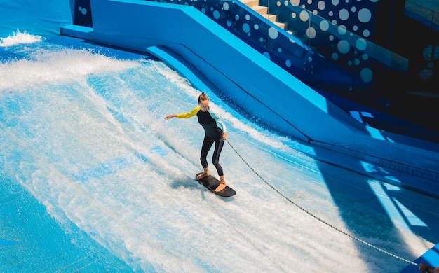 Beautiful young woman surfing on a wave simulator at a water amusement park