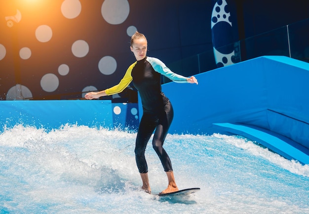 Beautiful young woman surfing on a wave simulator at a water amusement park