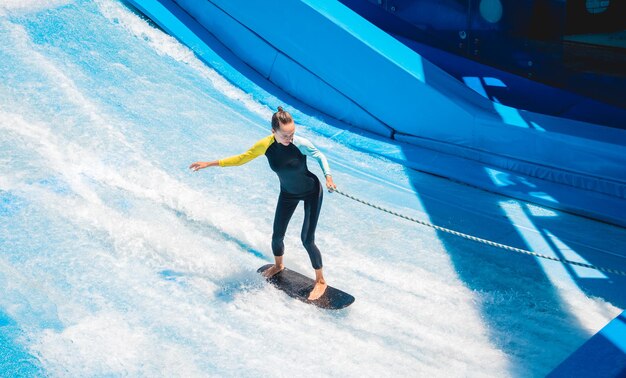 Beautiful young woman surfing with trainer on a wave simulator at a water amusement park