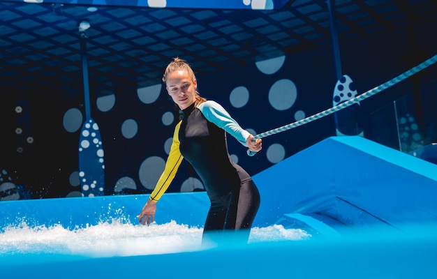 Beautiful young woman surfing with trainer on a wave simulator at a water amusement park