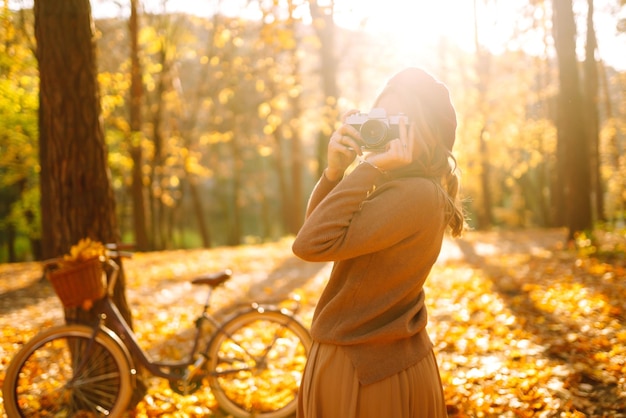 美しい若い女性が秋の森でレトロカメラで写真を撮り秋の天気を楽しんでいます
