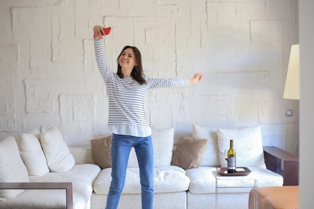 Photo beautiful young woman taking selfie with smartphone at home near the couch