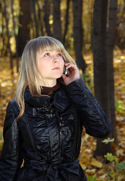 秋の公園で電話で話している美しい若い女性