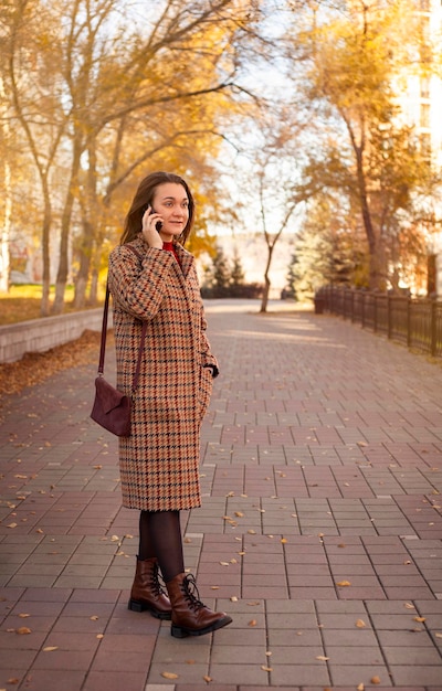 Beautiful young woman talking on the phone in the autumn park