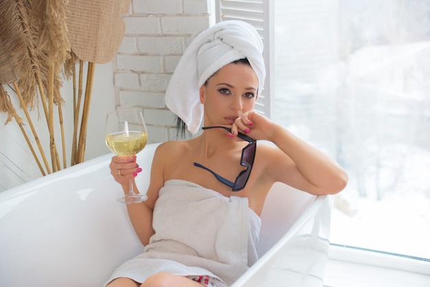 Beautiful young woman in a towel sitting on the edge of a champagne bath Selfcare and spa concept