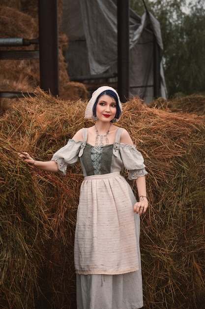 Photo beautiful young woman in a traditional bavarian costume is standing near the haystacks on the farm