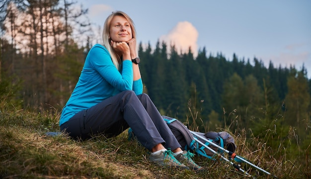 Beautiful young woman traveler sitting on grassy hill