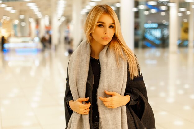 Beautiful young woman in a trendy gray coat with a stylish scarf in the mall