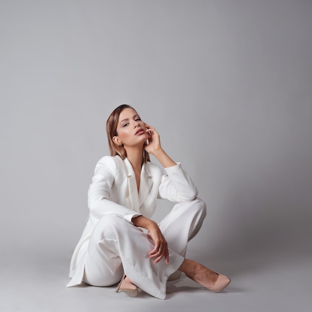 Beautiful young woman in a trendy white suit and beige highheeled shoes