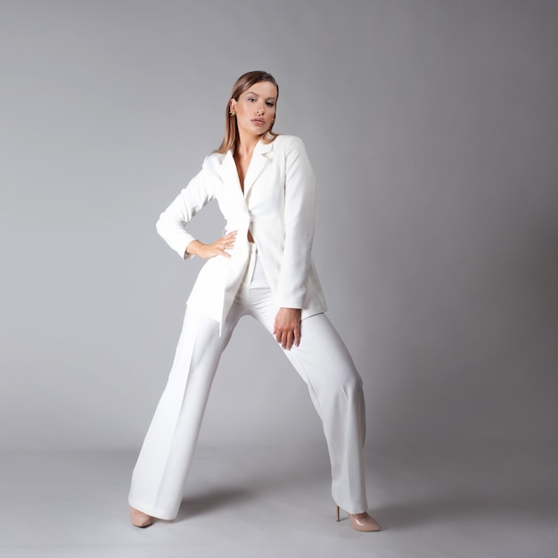 Beautiful young woman in a trendy white suit stands in a dynamic pose