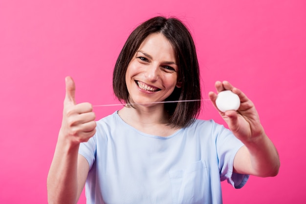 Beautiful young woman use dental floss on pink background