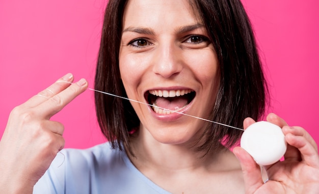 Beautiful young woman use dental floss on pink background