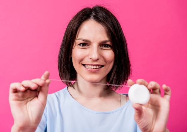 Beautiful young woman use dental floss on pink background