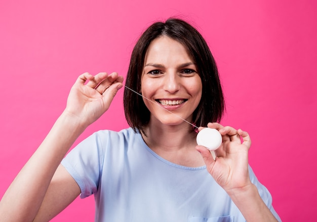 Beautiful young woman use dental floss on pink background