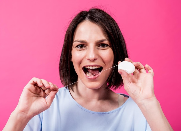 Beautiful young woman use dental floss on pink background