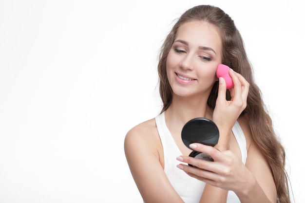 Beautiful young woman using beauty blender for applying foundation for make-up on face isolated on white background